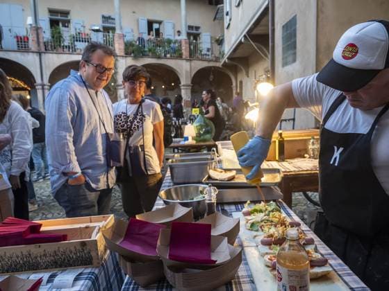 Il cuoco fa colare la salsa sui panini allineati sul marmo, la mano guantata sopra il banco, mentre due ospiti aspettano a un passo. Nel cortile con la loggia le lampadine sono accese e la luce del giorno sta finendo.